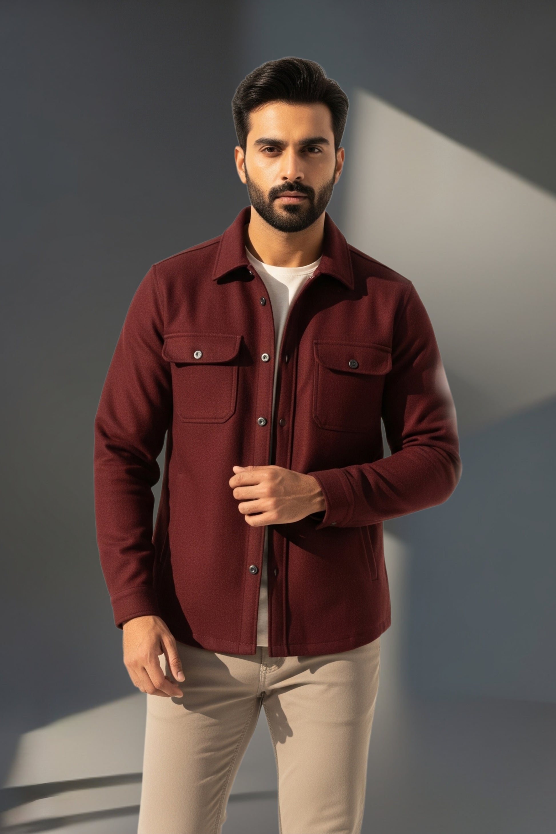 Man wearing a maroon shirt over a white t-shirt with beige pants against a gray background