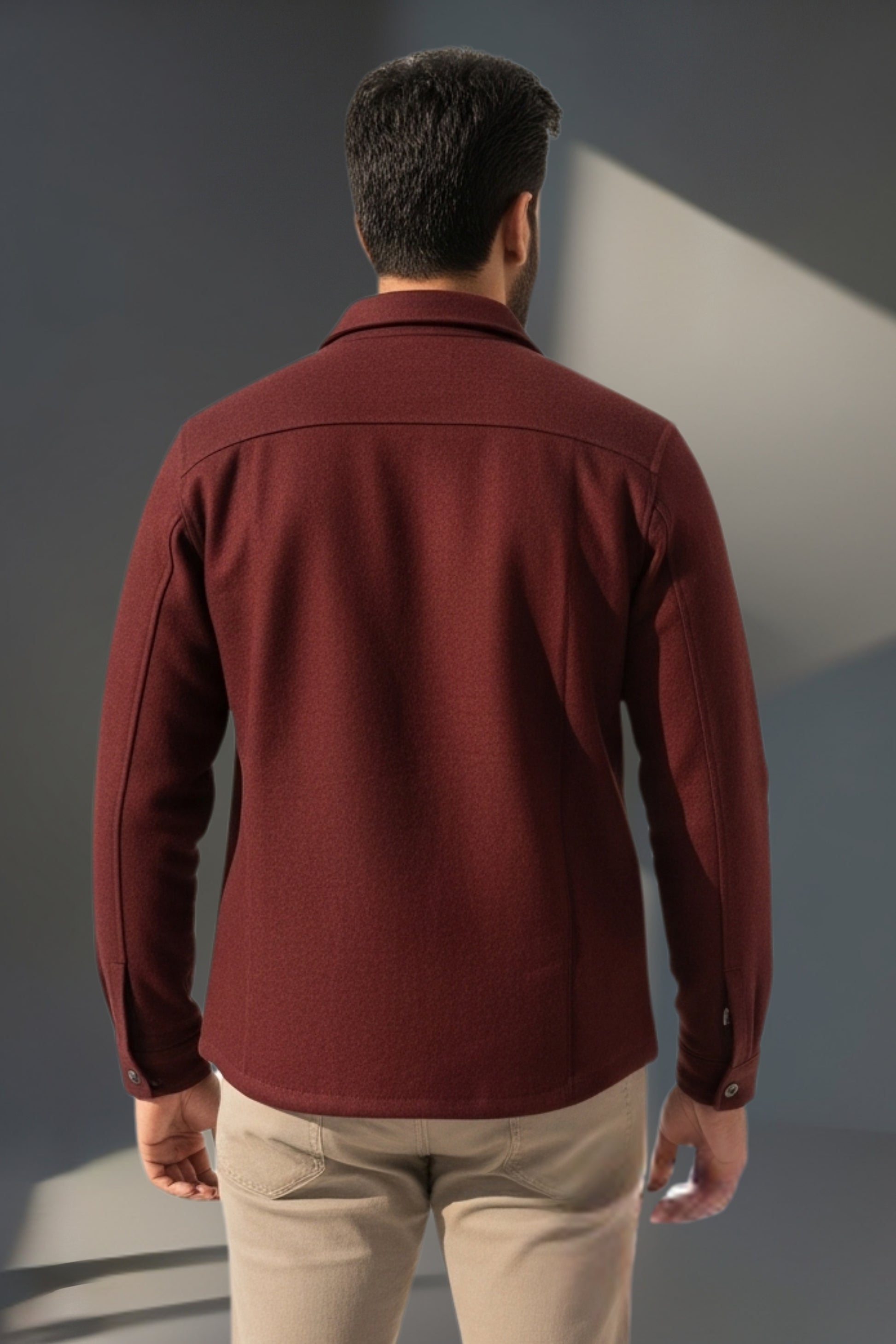 Man wearing a maroon jacket and beige pants against a gray background