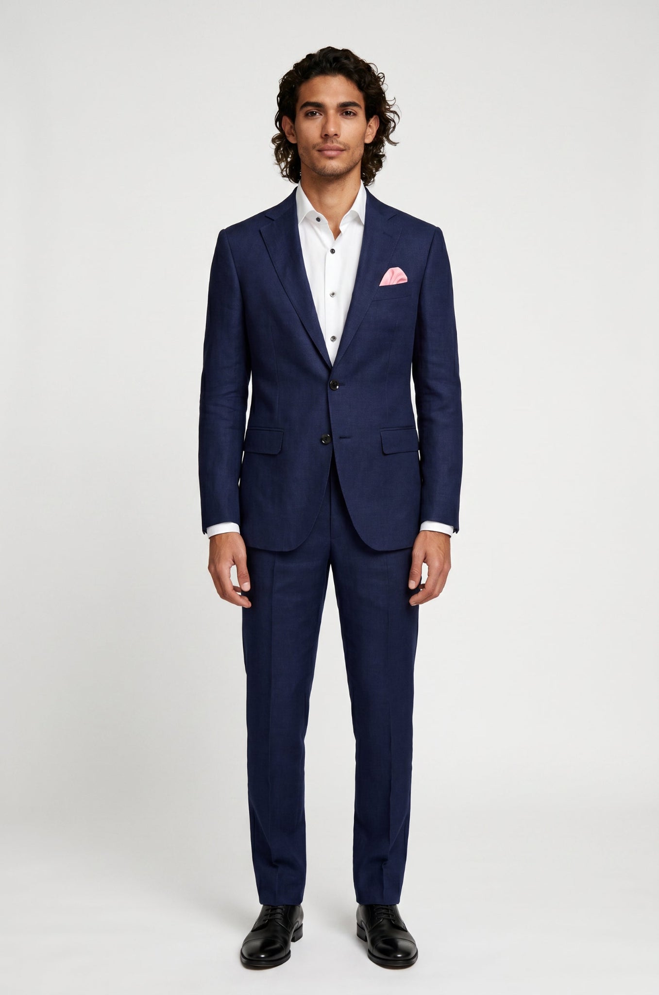 Man wearing a blue linen suit with a white shirt and pink handkerchief on a white background
