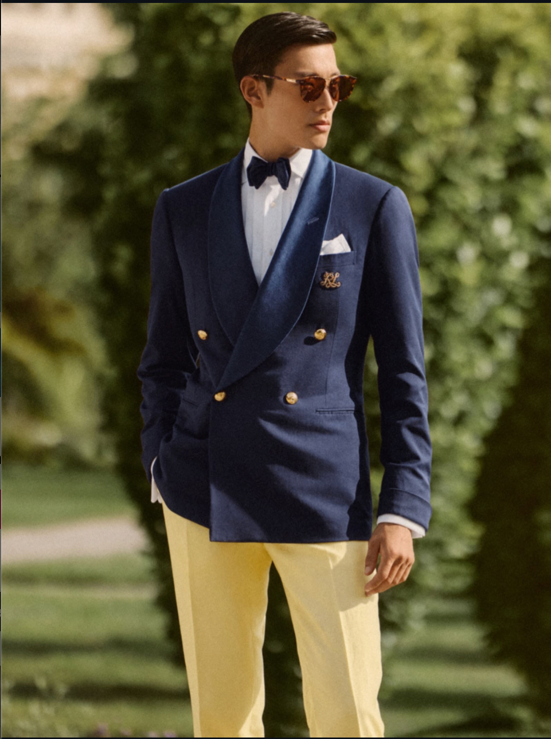 Man wearing a navy blazer with gold buttons, white shirt, and yellow pants outdoors.