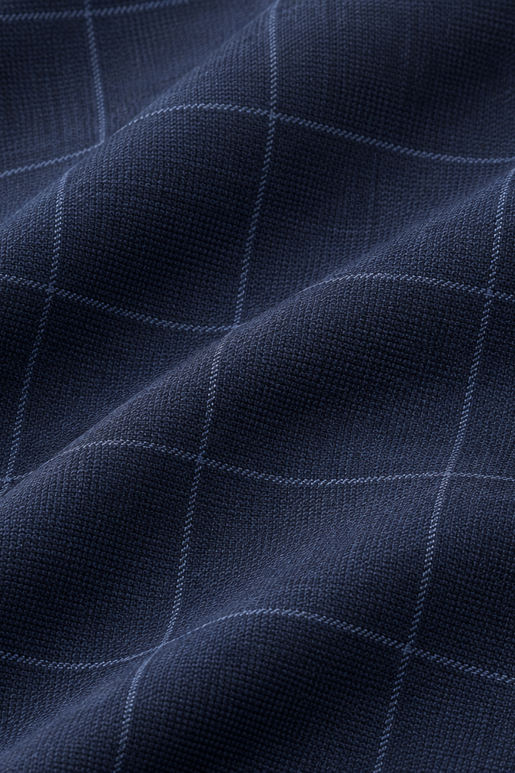 A close-up of dark navy blue fabric with a subtle light blue windowpane plaid pattern, showing soft folds and texture.